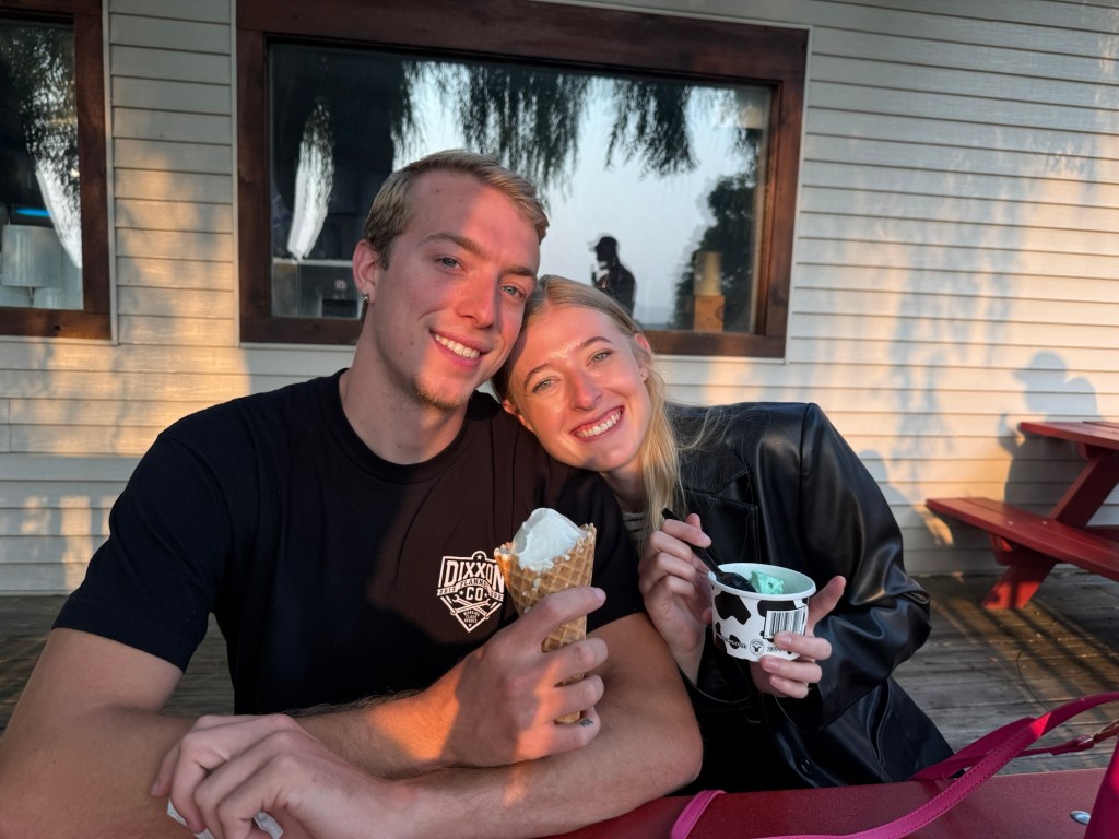A young couple enjoying ice cream together at an outdoor setting, smiling and posing for the photo.