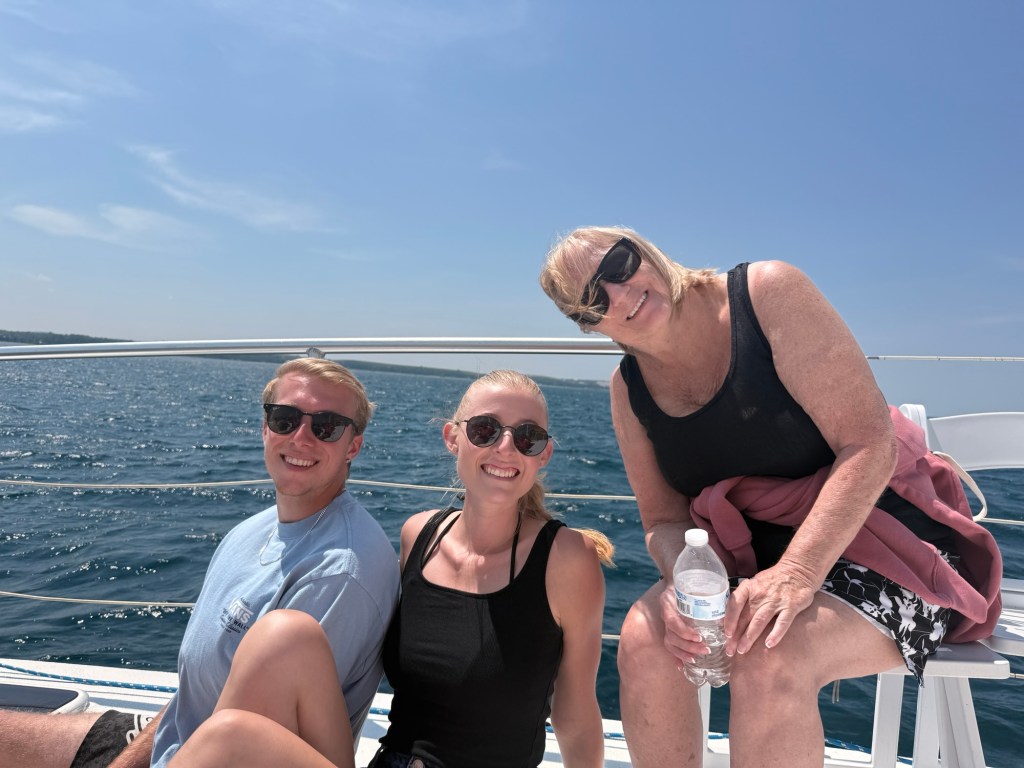 Three individuals smiling together on a boat, enjoying a sunny day by the water.