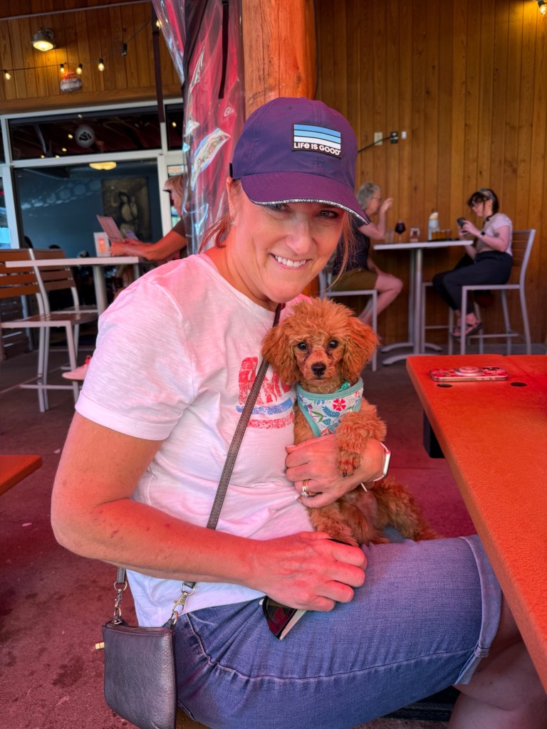 A woman sitting at a restaurant, happily holding her toy poodle puppy, both enjoying their time together.