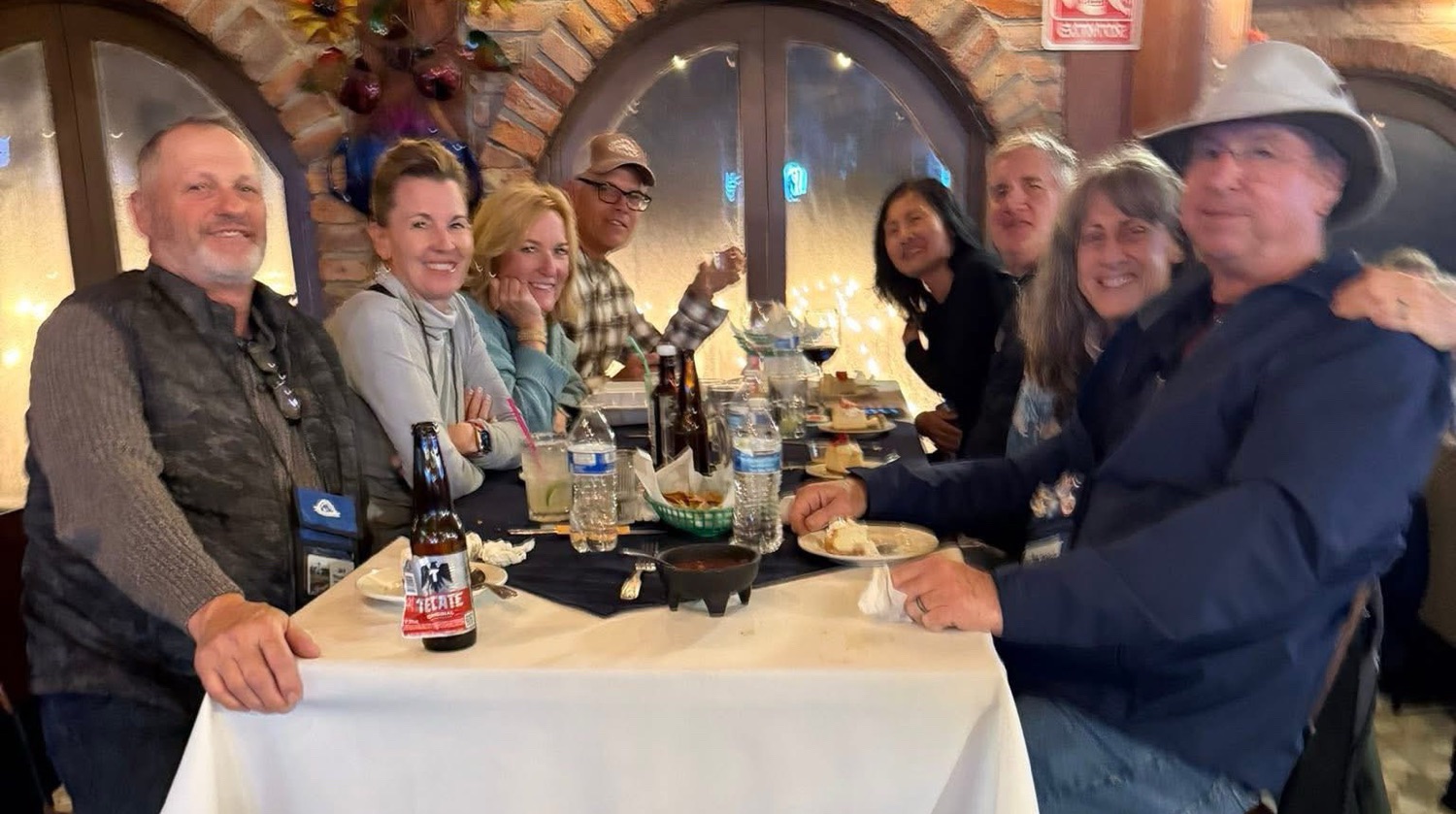 Group of eight people seated at a table enjoying a meal and drinks in a cozy restaurant setting.
