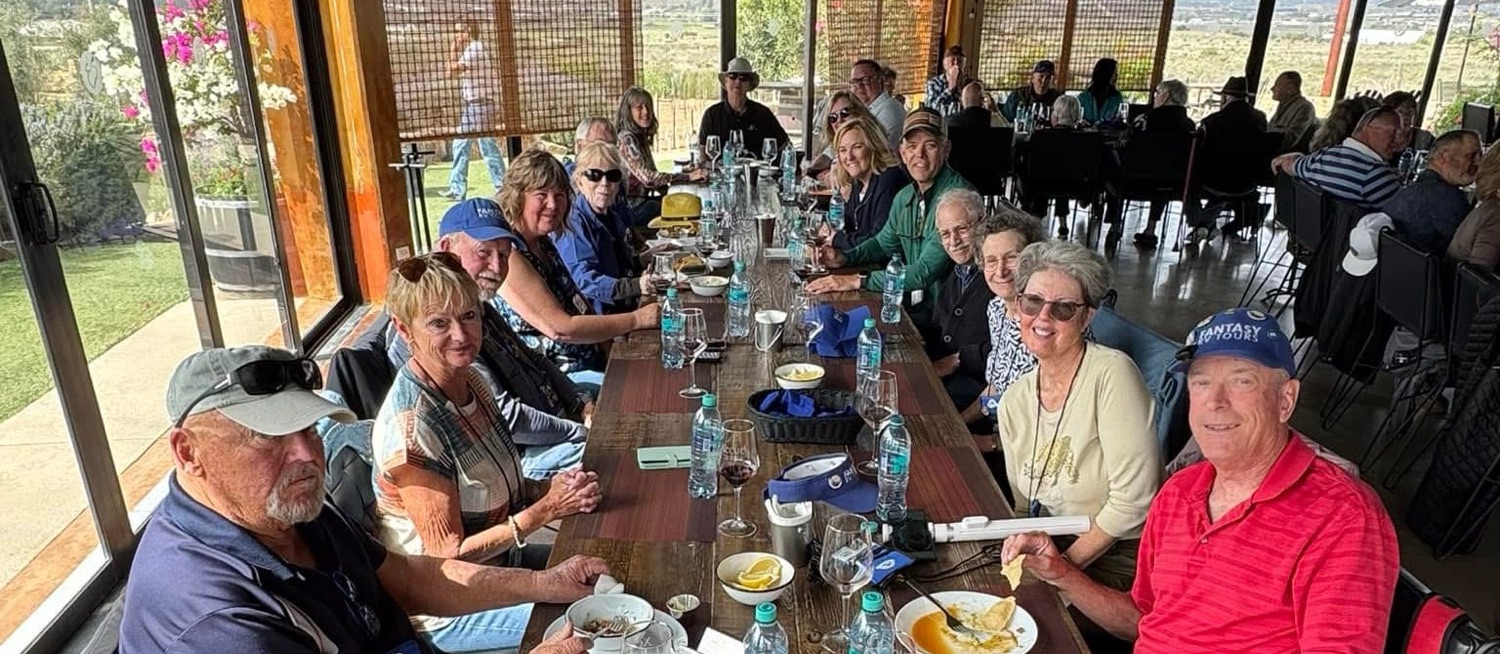 A group of people seated around a long table in a restaurant, enjoying a meal together with drinks and food in front of them.