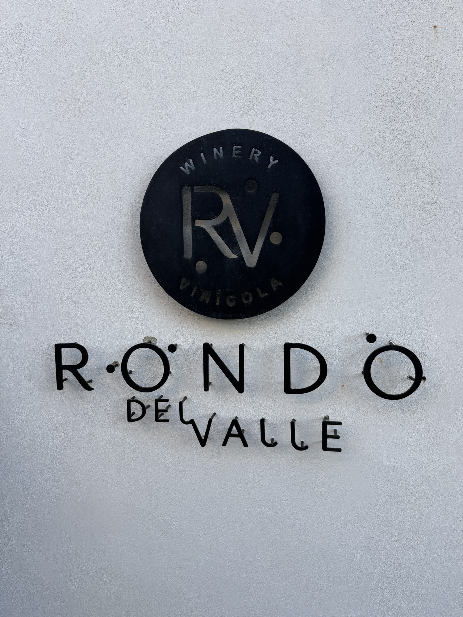 Sign for Rondo del Valle winery featuring a circular logo with the initials RV and the word 'WINERY' above it.