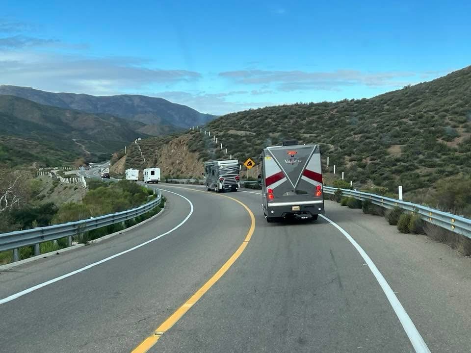 A winding road in a mountainous landscape with multiple RVs traveling in the same direction.