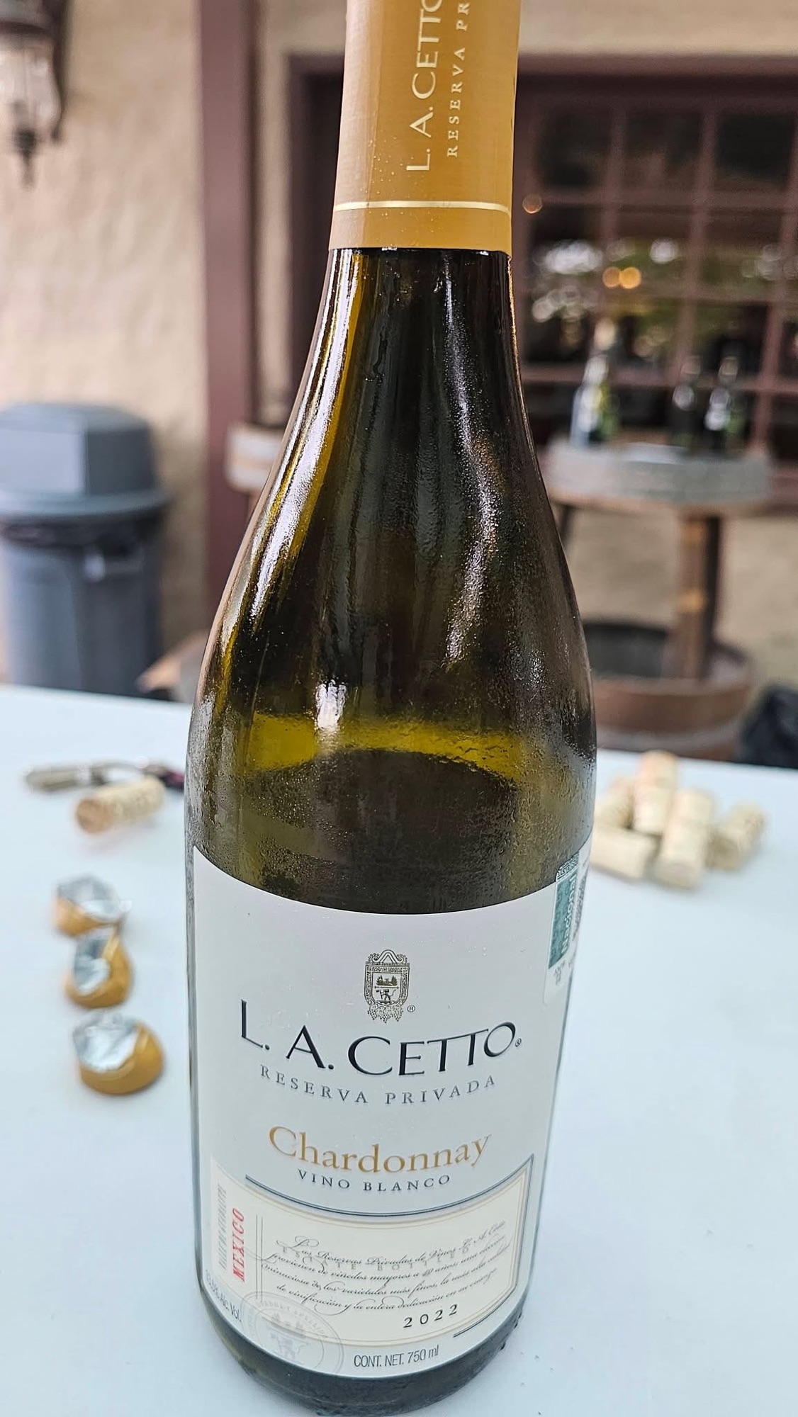 A bottle of L.A. Cetto Chardonnay Vino Blanco, 2022, displayed on a table with wine corks and caps in the background.